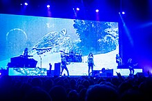 Six membres d'un groupe de rock jouant devant un écran présentant une tortue marine devant un public.