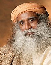 A headshot of Sadhguru looking into the camera with his head slightly tilted
