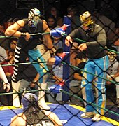 Picture of two masked men standing on the outside of the apron of the ring watching the match.