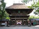 A two-storied wooden gate with a large thatched roof and a veranda with handrail on the upper floor.