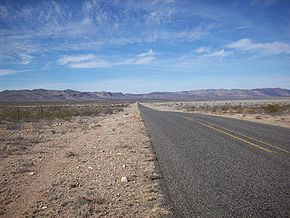 An image of straight stretch of FM 2017 passing through treeless shrub land. Mountains of the Sierra Vieja range are in the distance.