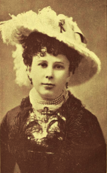 19th-century B&W portrait photo of a woman wearing a large hat and a dark jacket.