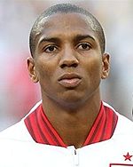 The head and shoulders of a young man with short hair. He is wearing a white top with red trim. The top features a crest with three lions on it, and a small star above it.