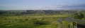 Photograph of the Bear River Massacre Site, a wide, open grassland with scattered trees, low hills in the background, and a highway alongside.