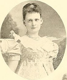 19th-century B&W oval portrait photo of a woman with her hair in an up-do, wearing a pale, short-sleeve dress.