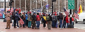 A crowd carrying multiple American flags outside. There is a Thin Blue Line flag in the center.