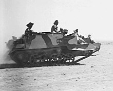 A tracked military vehicle moves across the desert