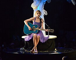 Swift playing a guitar, sitting under an artificial tree