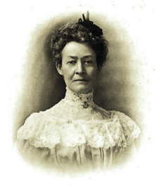 B&W portrait photo of a woman with her hair in an up-do, wearing a pale-colored frilly blouse.