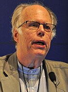 A close-up of man older man with glasses speaking at a conference