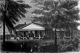 house with columns in the front, two trees- one right, one left- in foreground, figures walking on porch of building and in foreground.