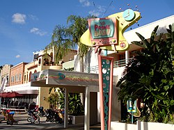 A photograph of a white building with a pink, green, and yellow television-shaped sign in front of it reading "50's PRIME TIME Cafe" in stylized letters