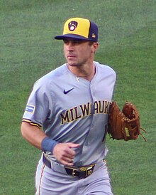 A man in a gray baseball uniform and a blue and yellow hat running on a baseball field