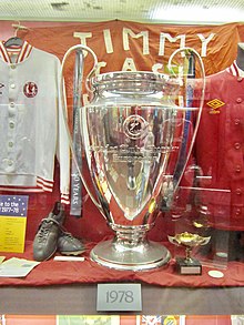 Grande coupe argentée présentée au milieu d'autres souvenirs dans une vitrine de musée.