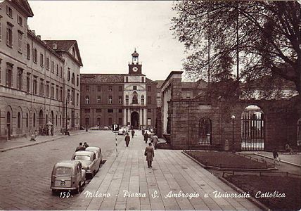 Photographie en noir et blanc d'une rue avec des bâtiments en face et à gauche et un par-terre sur la droite.