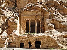 A colonnades classically styled temple carved out of a beige-colored rock cliff face.