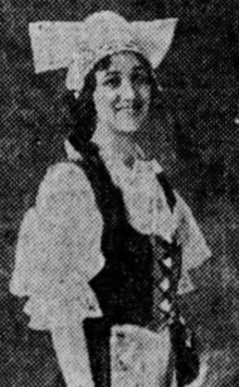 A smiling young white woman with dark hair, wearing a European folk costume with a white cap and a white blouse with poofy sleeves