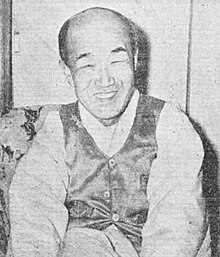 Grainy black and white photograph of Kim Yun-kyong aged 67 and balding. He is sat down and wearing a tuxedo and looks very happy with a huge smile on his face.