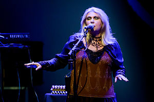 Singer with eyes closed, arms stretched forward slightly, palms down, appears to be floating on the music as she sings.