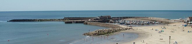 Vue panoramique. La pleine mer et un port bien protégé par sa jetée.