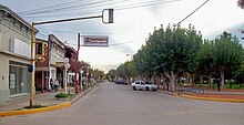 View down a street with shops on one the left and a tree-lined park on the right