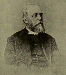 A historical black-and-white portrait of a man with a beard, wearing a suit and bow tie, facing to the right.