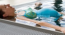 A pregnant woman floats in the corner of a swimming pool