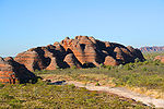 Large red sandstone rock formation surrounded by shrubbery and open plains