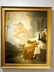 A barefoot nun looking up to angels and a dove. She sits by a table. Other nuns enters through a side door.