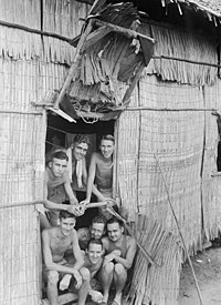 Shirtless and malnourished men smiling in a in the doorway of a hut