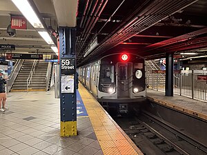 Uptown platform of the IND station. There are tracks on either side of the platform. To the right is a blue column containing a sign with the words "Columbus Circle". In the background is a staircase.