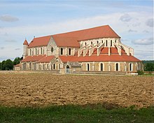 Photo d'une église monumentale de style gothique primitif en pierres blanches et jaunes et toits en tuiles rouges.