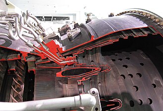 JT9D straight-through annular combustor, airflow from left to right. The atomizing fuel nozzle is a dual orifice or duplex type. The primary, or pilot flow, comes from a small hole (orifice) in the centre at low engine speeds through the fuel tube at the left. The secondary, or main flow, comes from a larger opening around it at higher speeds through the tube on the right. Airflow from the small compressor exit guide vane at the left enters an area-increasing diffuser which divides it into three parts. The centre flow enters the combustor and mixes with fuel. The outer and inner parts enter the combustor progressively through the holes shown completing the combustion and then diluting to give a final exit temperature suitable for the turbine.