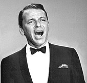 Black-and-white photo of a man in a tuxedo is singing