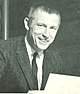 Jerry Burns wearing a suit and tie, holding a piece of paper