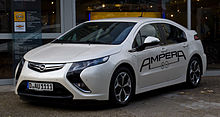 Front 3/4 view of a Navajo-White colored automobile with large, black labelling that says AMPERA