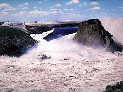 Vue de la brèche dans le barrage Teton le 5 juin 1976 : la retenue (en arrière-plan) se vide entre la paroi rocheuse (à gauche) et ce qui reste du barrage (à droite).