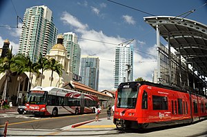 A Rapid bus departs Santa Fe Depot station (left) while a Blue Line train of the San Diego Trolley loads passengers at America Plaza station. The stations are a major MTS hub in downtown San Diego.