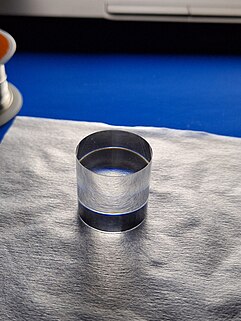 A crystal cylinder rests on a piece of white cloth, which itself sits on a blue surface of a table.