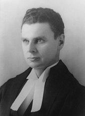 Diefenbaker with an intense look in his eyes. Still a young man, he wears ceremonial robes in this portrait shot; the bands of the robes are visible.