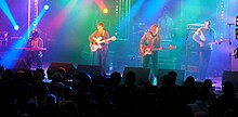 The band onstage with colored lights shining around them