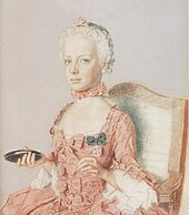 Solemn-faced girl child in a pink dress decorated with bows. Facing half-left, she carries an object in her right hand that might be a compact, or a mirror.