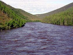 A choppy river is seen surrounded by tree-covered hills.