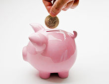 A hand putting a one-dollar coin into a slit on the top of a pink pig-shaped ceramic container.