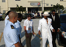 Usher in a white source with a small entourage, walking in a parking lot