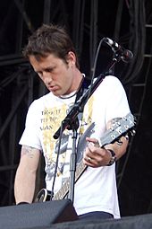 A man in a white shirt plays a guitar atop a stage.