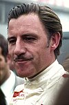 Graham Hill in white racing overalls and looking to the right of the camera