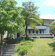 Zeigler House perched on a hill viewed from street level with front door at left. House is partially obscured by two trees.