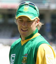 A cricketer in a green top, wearing a baseball cap