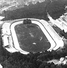 photographie en noir et blanc d'un stade entouré de tribunes, une piste d’athlétisme entoure la pelouse